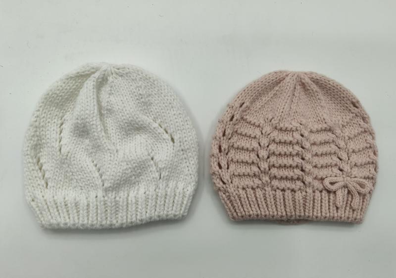 Two hand-knitted baby beanies side by side, white with leaf pattern and blush pink with horizontal texture and bow detail