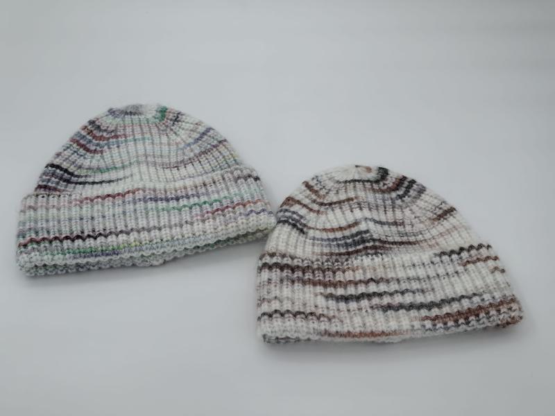 Two hand-knit ribbed beanie hats in white with multicolor stripes, one with cool tones and one with warm earth tones, on white background