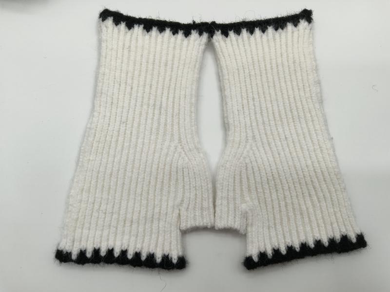 Flat lay of handknitted white ribbed fingerless mittens with black contrast trim at cuffs and wrist openings