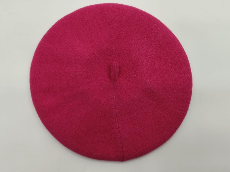 Flat lay of a hot pink fine knit wool beret with center button top on white background