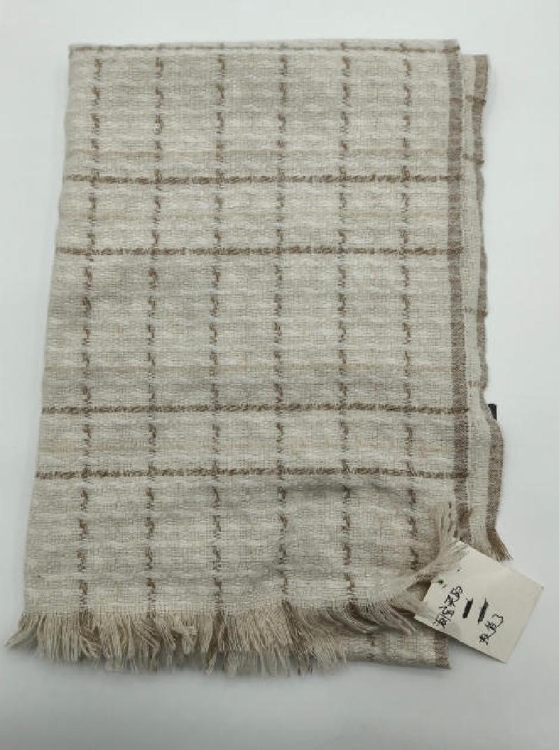 Folded ivory and beige woven plaid throw blanket with fringe trim and textured grid pattern