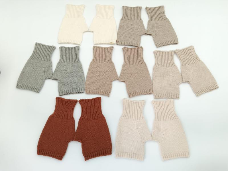 Seven pairs of handknit baby bloomers in cream, gray, taupe, beige, rust, blush, and sand laid flat on white background