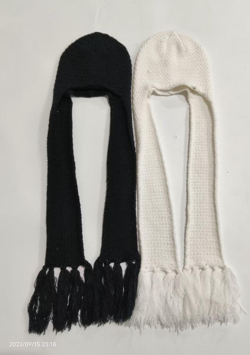 Two knitted hooded scarf hats with long tasseled ends laid flat, one black and one white, earflap balaclava winter style