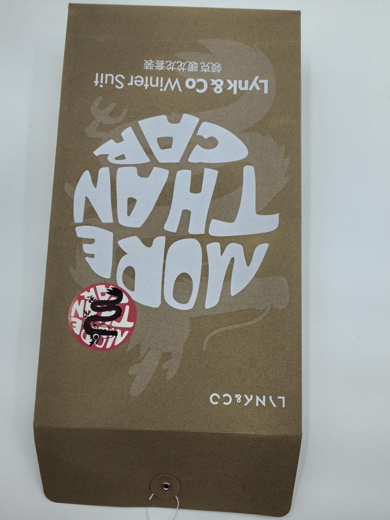 Upside-down kraft brown gift box printed with 'More Than Core' text, dragon sticker, and Lynk & Co Winter Suit branding