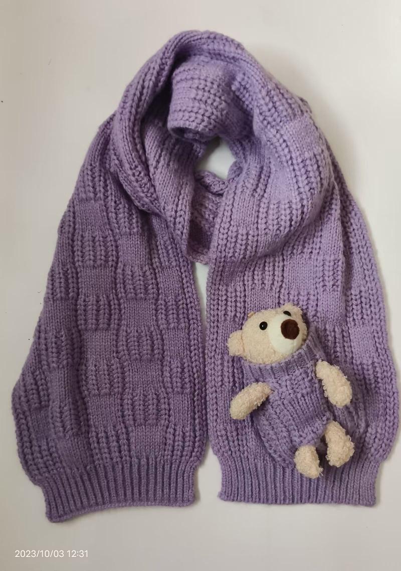 Purple lavender chunky knit scarf laid flat with a small cream teddy bear plush peeking out of a knitted pocket