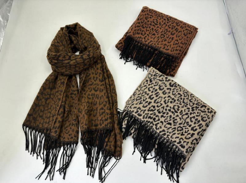 Three leopard print scarves with black fringe in dark brown, caramel brown, and beige colorways laid flat on white surface