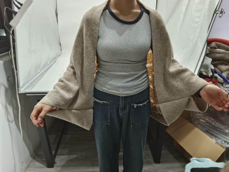Woman wearing an oversized beige knit open-front cardigan over a grey ribbed top with blue denim jeans